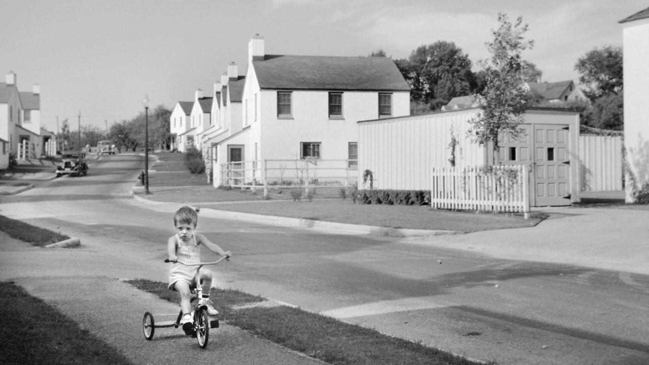 Alte Aufnahme einer Straße mit frisch erbauten kleinen Reihenäusern. Im Vordergrund ein kleiner Junge auf einem Dreirad.