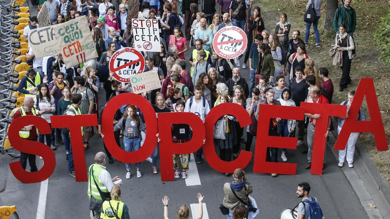 Die Demonstranten laufen eine Straße entlang und tragen die Buchstaben "Stop Ceta".