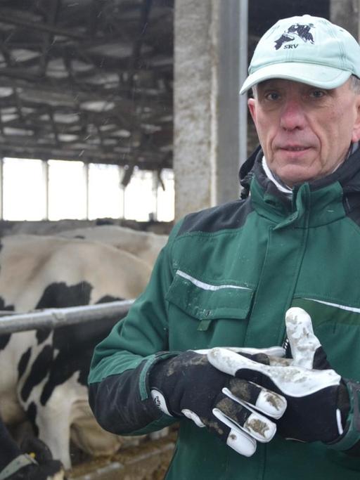Tierwirt Thomas Druskat steht in Arbeitskleidung vor seinen Kühen im Stall