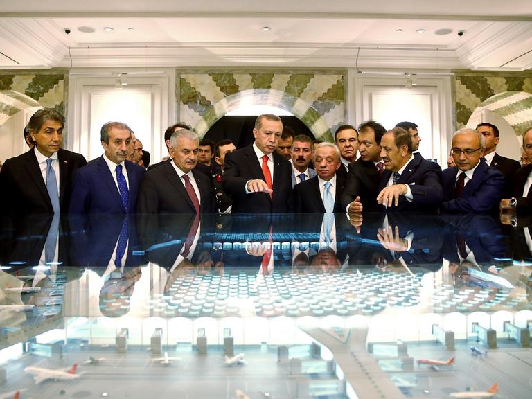 Der türkische Präsident Recep Tayyip Erdogan steht in einer Gruppe von Männern bei der Unterschriften-Zeremonie der "Istanbul New Airport Project Financing" am 19.10.2015 in Istanbul vor einem großen Modell des Flughafens.