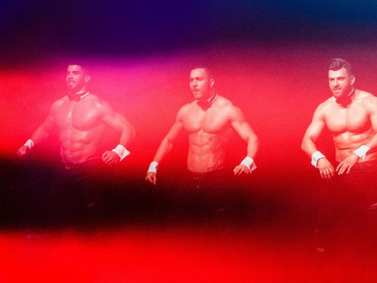 Drei Tänzer der Chippendales, getaucht in rote Lichtsäulen, performen 2017 in Hamburg im Mehr! Theater am Großmarkt.