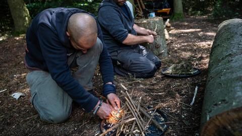 Teilnehmende eines Survivalkurses entfachen ein Feuer