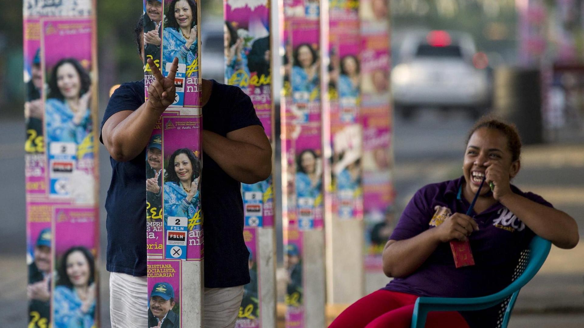 Eine lachende Frau versteckt sich hinter Wahlwerbung in Nicaragua.