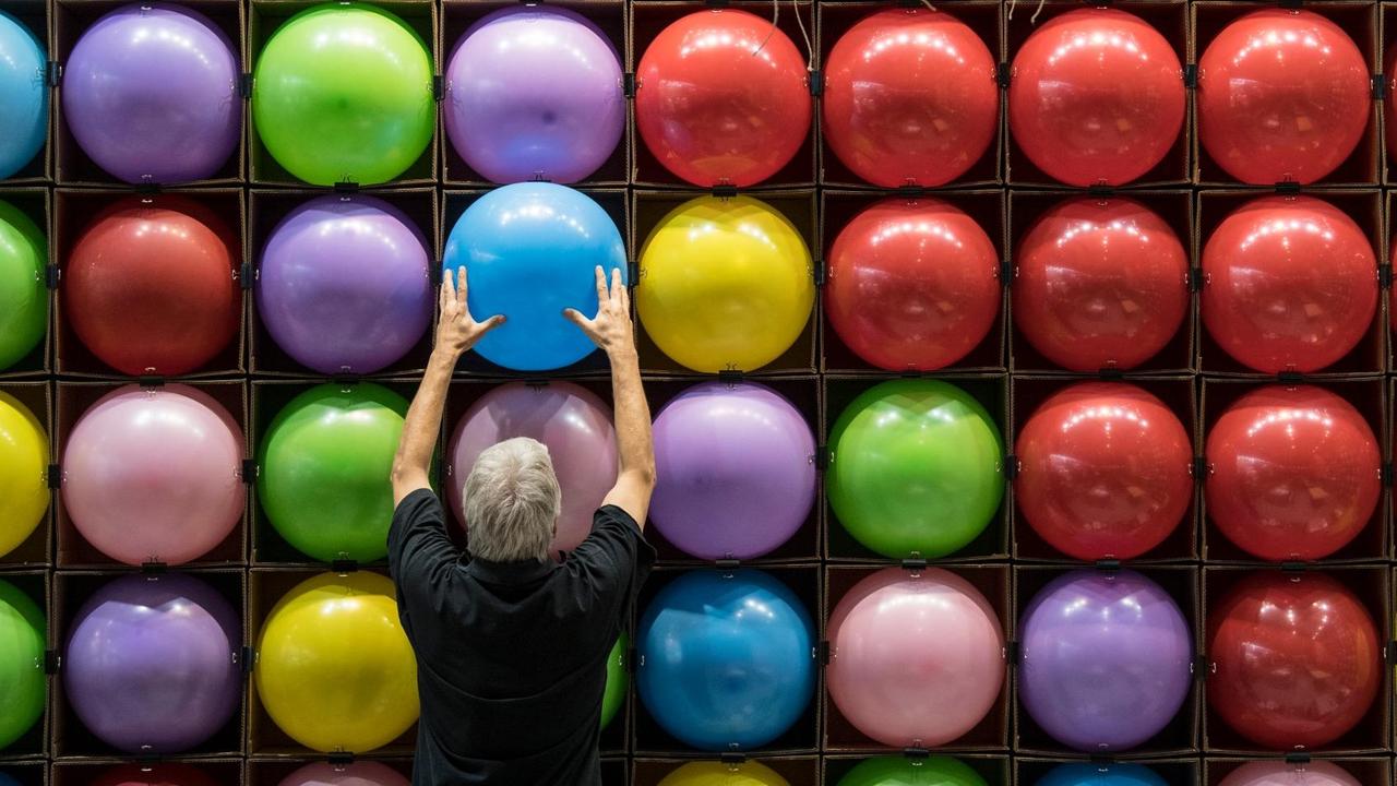 Zur Dekoration eines Standes bringt ein Messebauer zahlreiche bunte Luftballons an eine Wand an.
