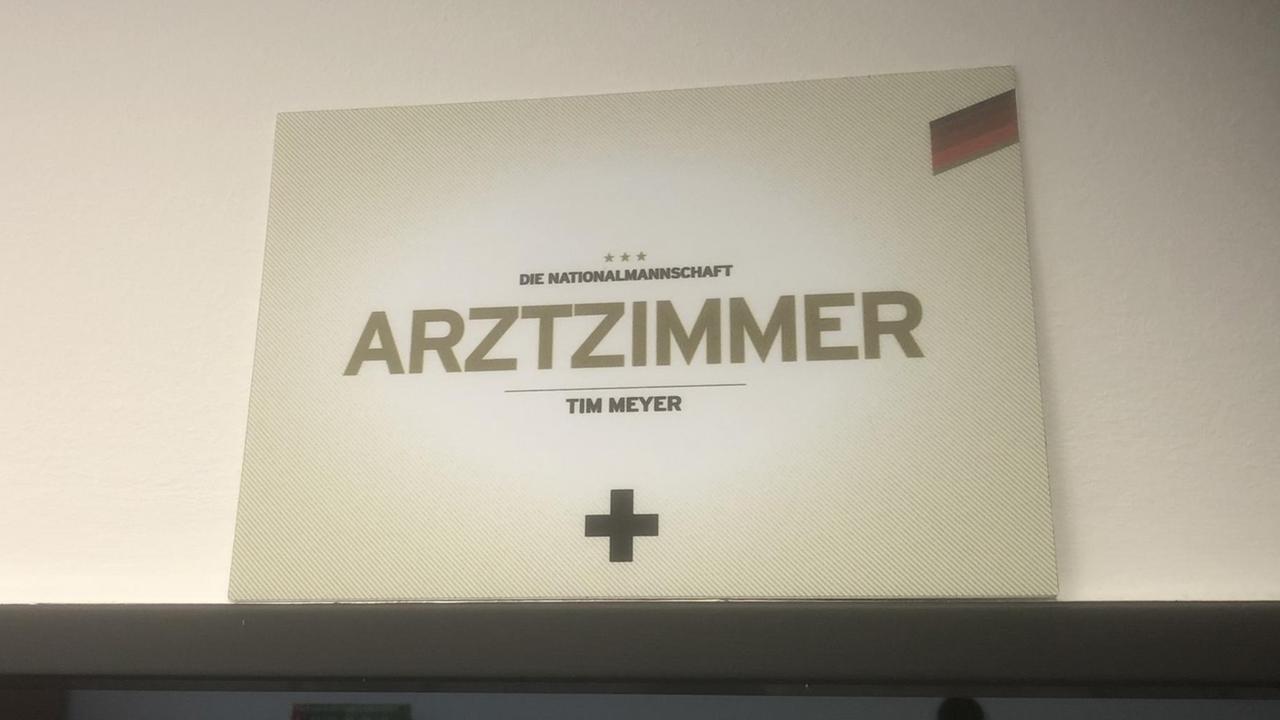 Schild mit der Aufschrift: "Arztzimmer". Darüber: "Die Nationalmannschaft". Darunter: "Tim Meyer"