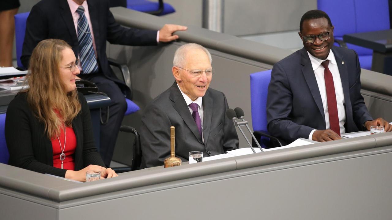 Schäuble lächelt ins Plenum, links von ihm und hinter ihm zwei weitere Personen.