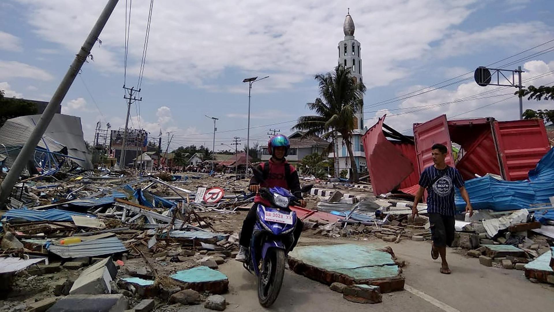Ein Fußgänger und ein Motorradfahrer bahnen sich in Indonesien den Weg durch eine Straße voller Schutt.
