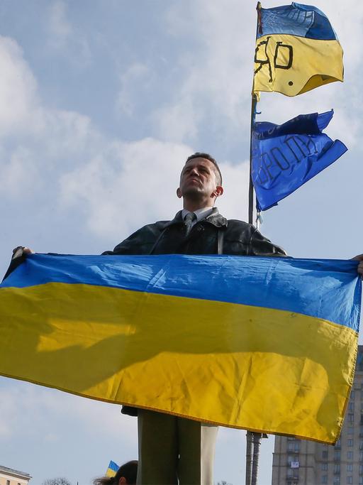 Ein Ukrainer hält in Kiew die Nationalflagge in die Höhe.