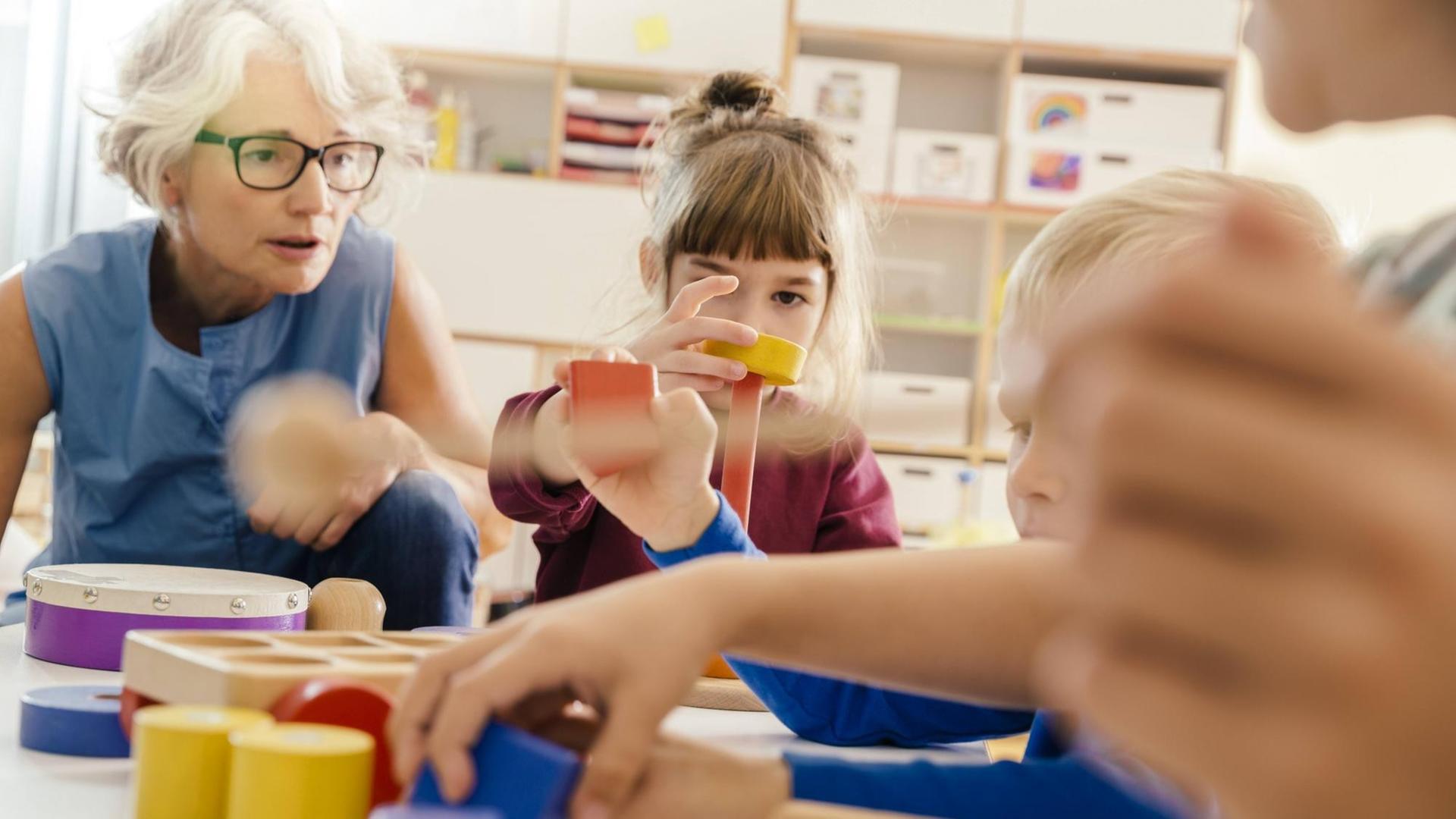Children and teacher playing with musical instruments and toys in kindergarten.