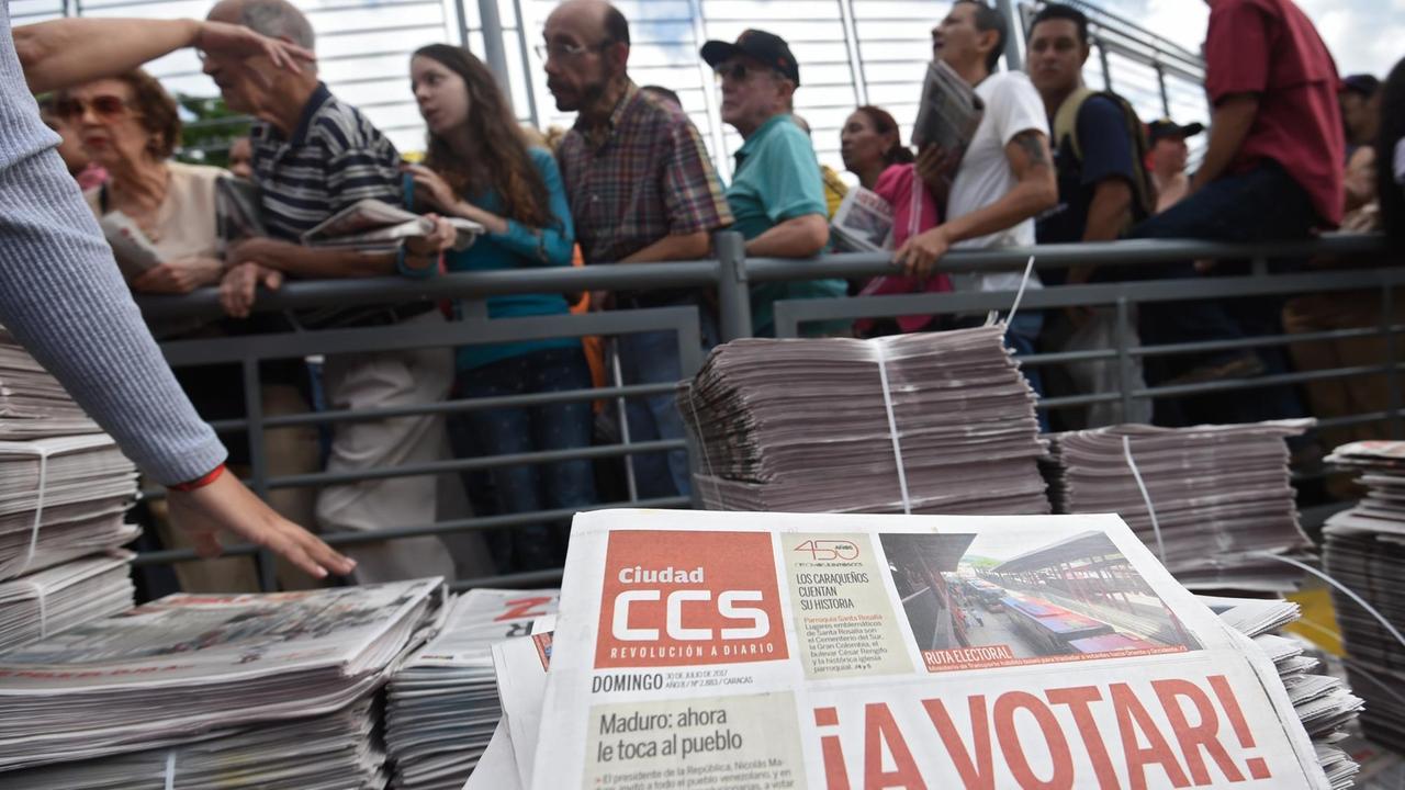 Menschen in Venezuelas Hauptstadt Caracas warten, um ihre Stimme bei der Wahl der Verfassungsgebende Versammlung am 30. Juli 2017 abzugeben. Im Vordergrund liegen Zeitungen, mit der Aufforderung, wählen zu gehen.
