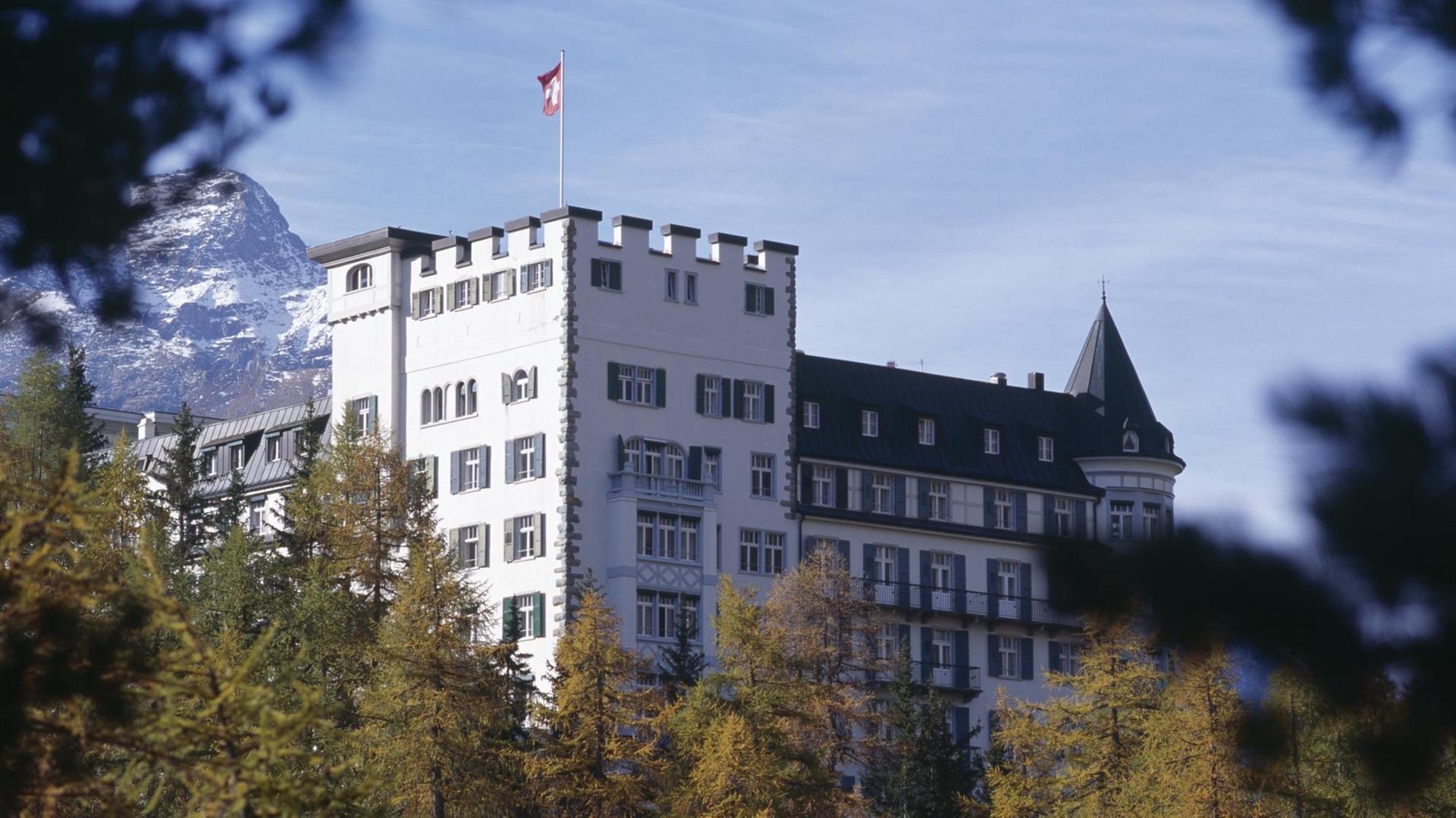 Das Waldhaus-Hotel in Sils-Maria im Kanton Grisons in der Schweiz hinter Baumwipfeln, dahinter Bergspitzen.