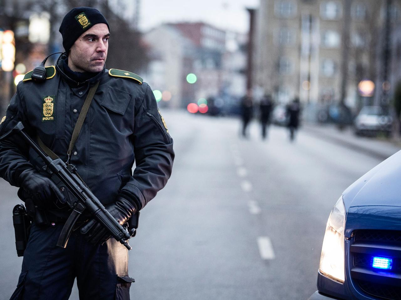 Ein bewaffneter Polizeibeamter steht neben einem Polizeifahrzeug.