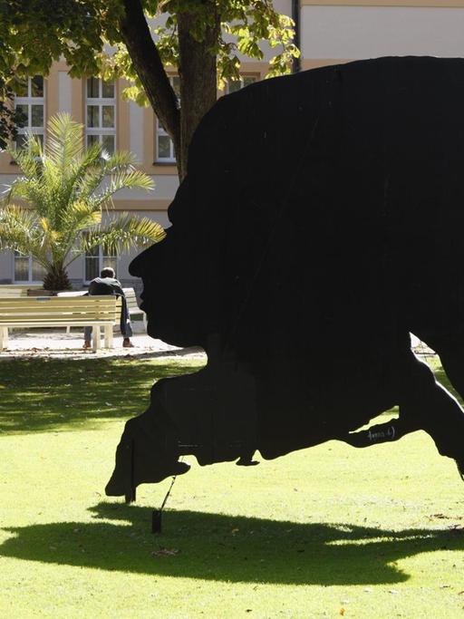 Ein großformatiger Schattenriss von Mozarts Kopf steht als Skulptur auf einer Wiese und wirft Schatten auf das umliegende Gras.