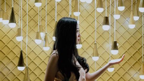 Eine Frau steht vor einer gelben Wand, vor der viele Energiesparlampen hängen.