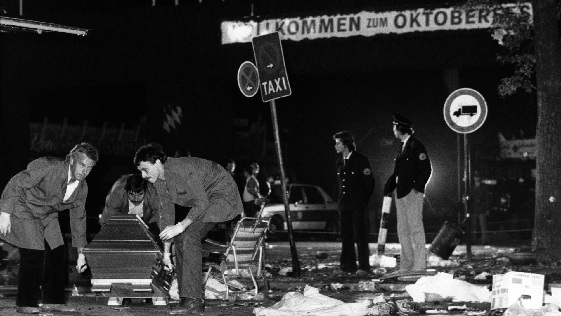 Ein Sarg wird nach dem Bombenanschlag auf dem Münchener Oktoberfest am 26.09.1980 vom verwüsteten Tatort weggetragen. Die Bombe befand sich vermutlich in dem Papierkorb an einem Verkehrsschild rechts im Hintergrund.