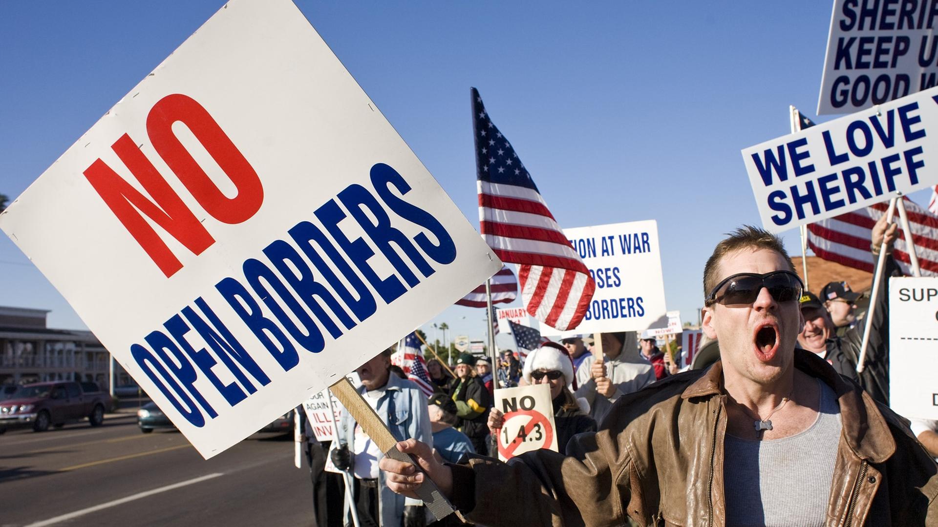 Demonstration in Phoenix gegen Immigration in die USA. "No open borders" steht auf einem Protestplakat, amerikanische Flaggen werden geschwungen.