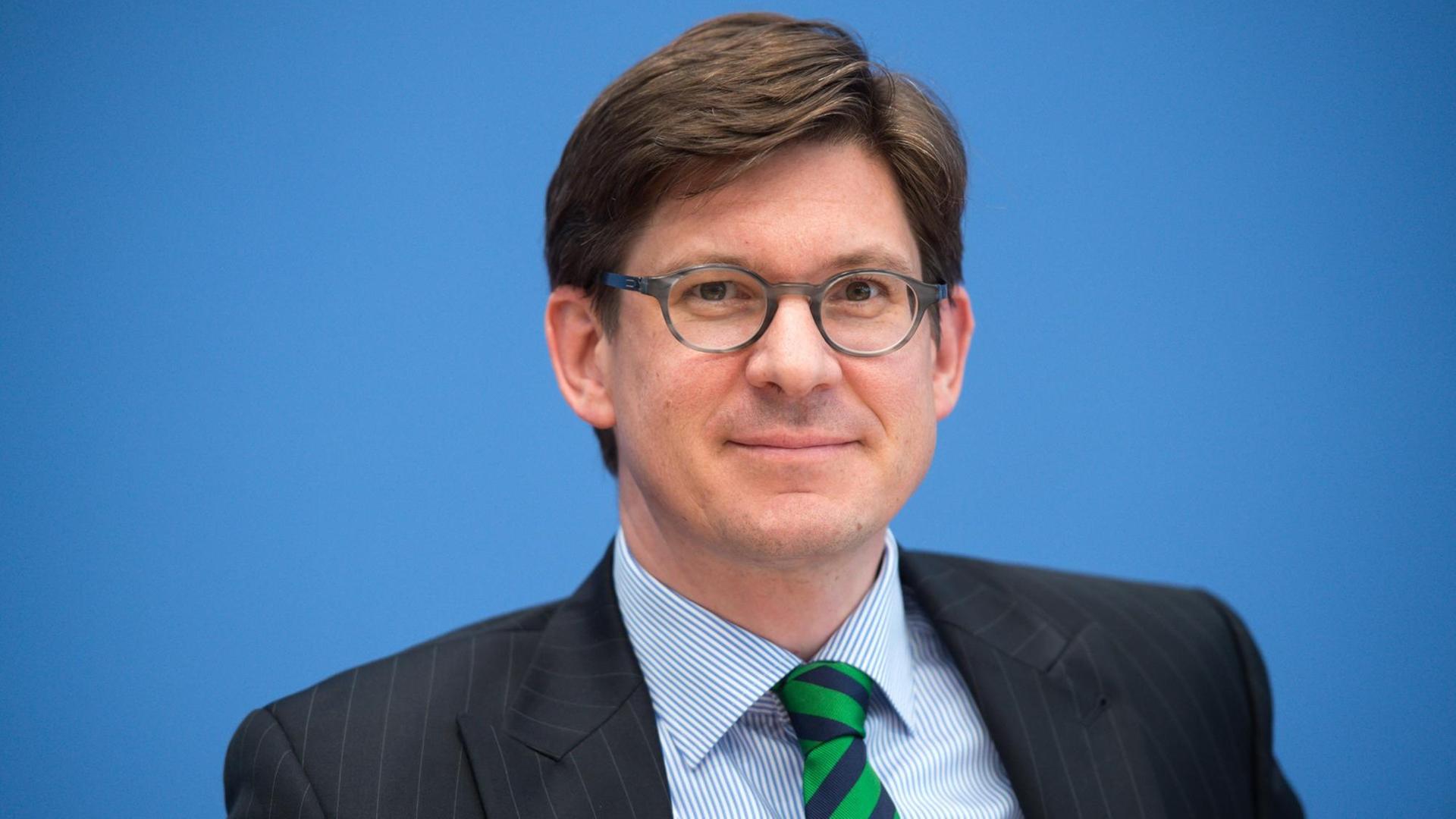 Ole Schröder, Parlamentarischer Staatssekretär im Bundesinnenministerium, in Anzug und mit Brille vor einer blauen Wand sitzend