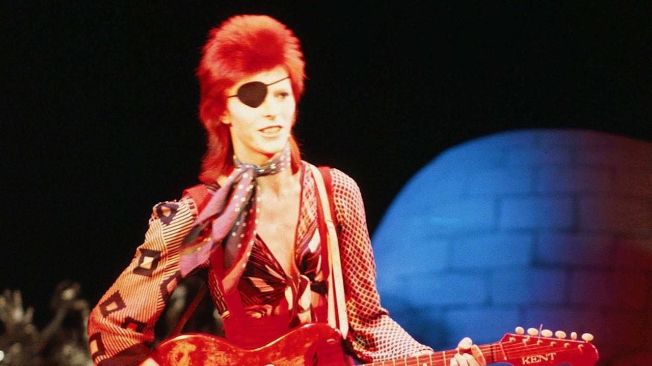 David Bowie mit Augenklappe und Gitarre.
