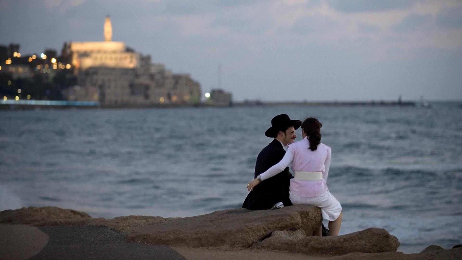 Ein juedisches Paar auf der Promenade am Strand vom Mittelmeer von Tel Aviv. Im Hintergund die Altstadt von Jaffa mit der Kirche St. Peter Church.