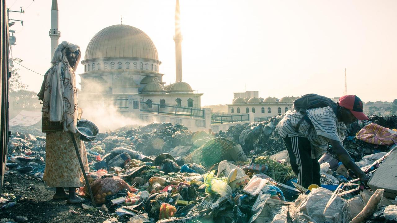 Conakry: Armut trotz Ressourcenreichtum. Menschen suchen im Abfall nach Verwertbarem. Im Hintergrund eine Moschee.