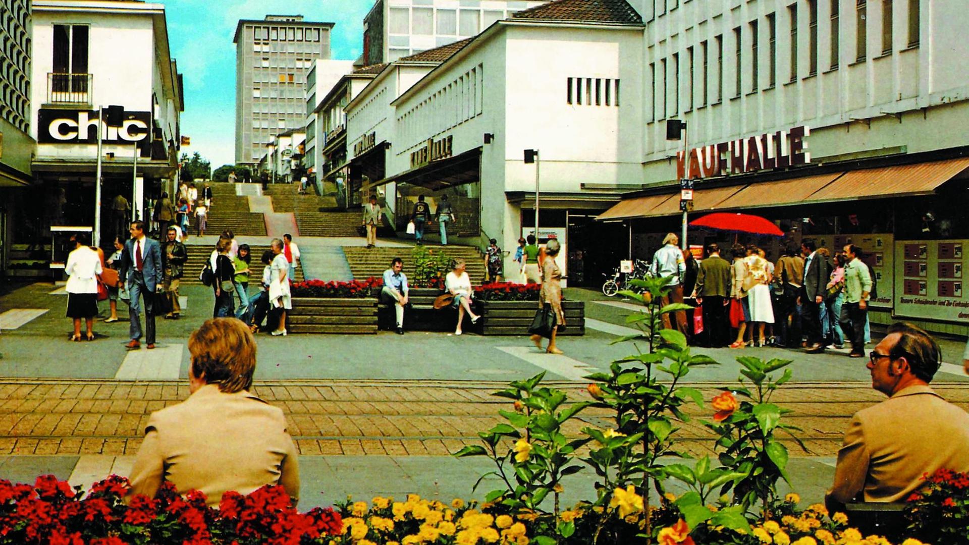 Ansichtspostkarte der Fußgängerzone "Treppenstraße" in Kassel mit Blumenkübeln im Vordergrund und den Treppen und Geschäften im Hintergrund. Farblich 70ger Jahre Charme.