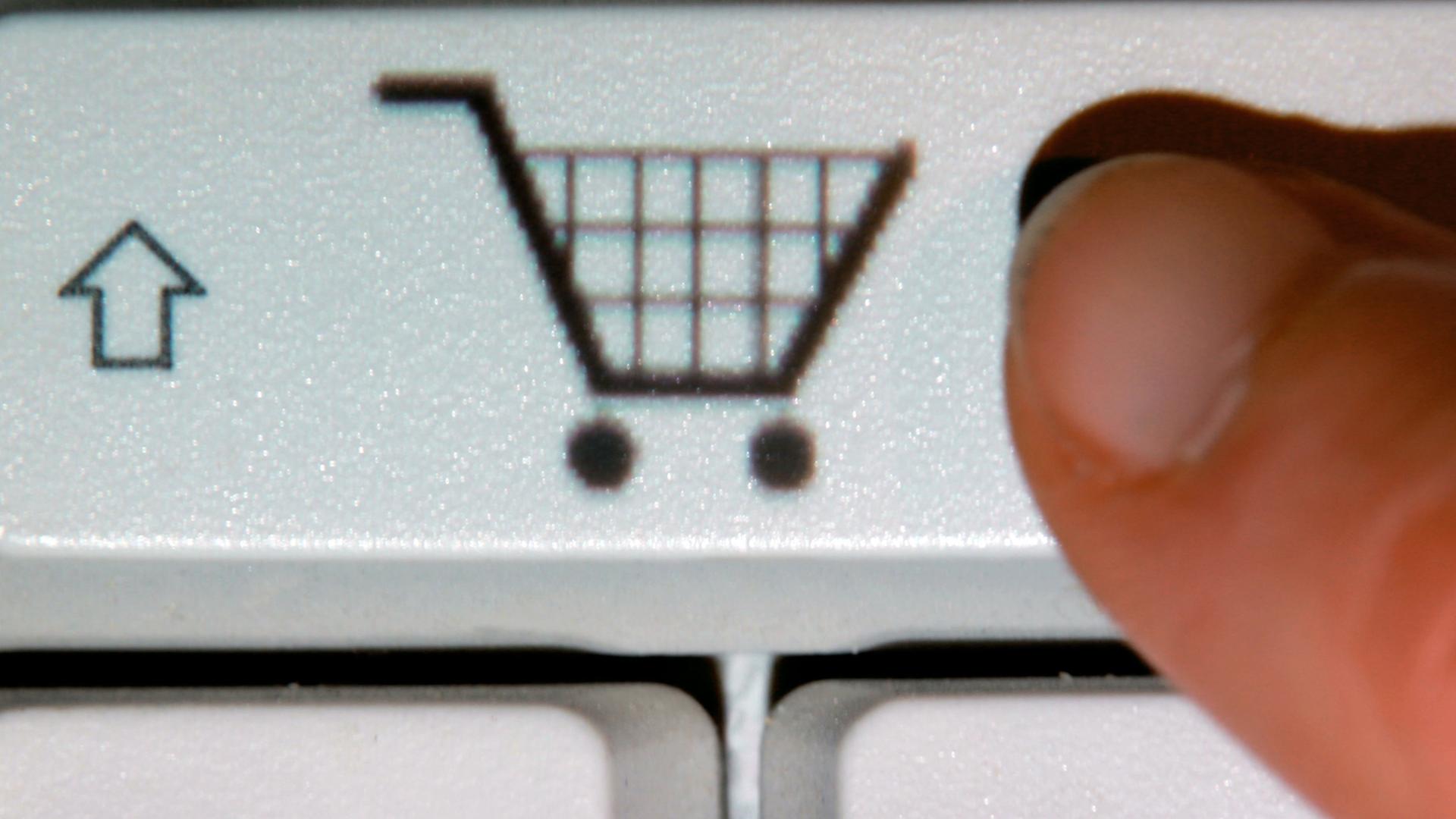 .Ein Finger zeigt auf das Symbol eines Einkaufwagens auf einer Taste einer Computertastatur.