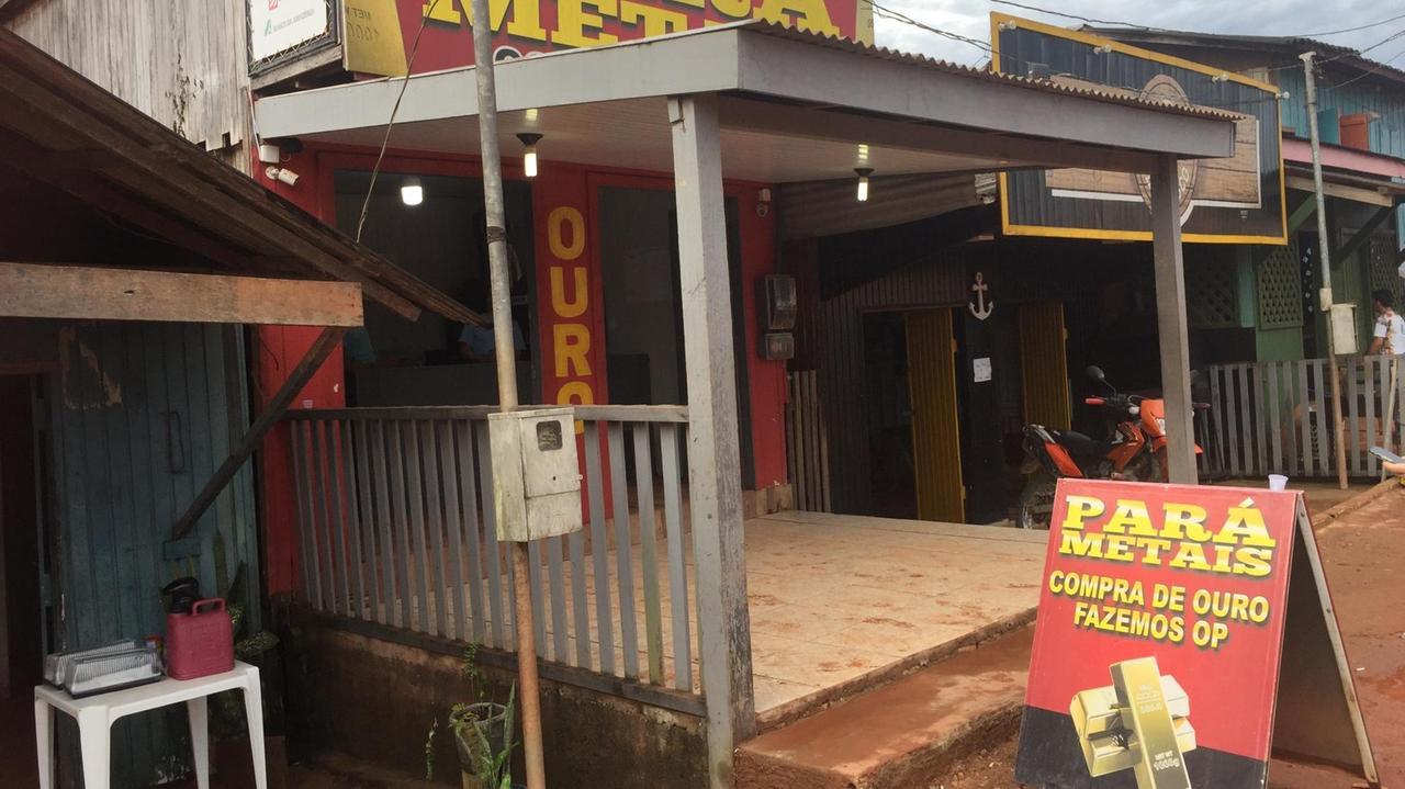 Ein unscheinbarer Laden in Creporizao vor dem ein rotes Plakat mit zwei Goldbarren Werbung für den Goldankauf macht..