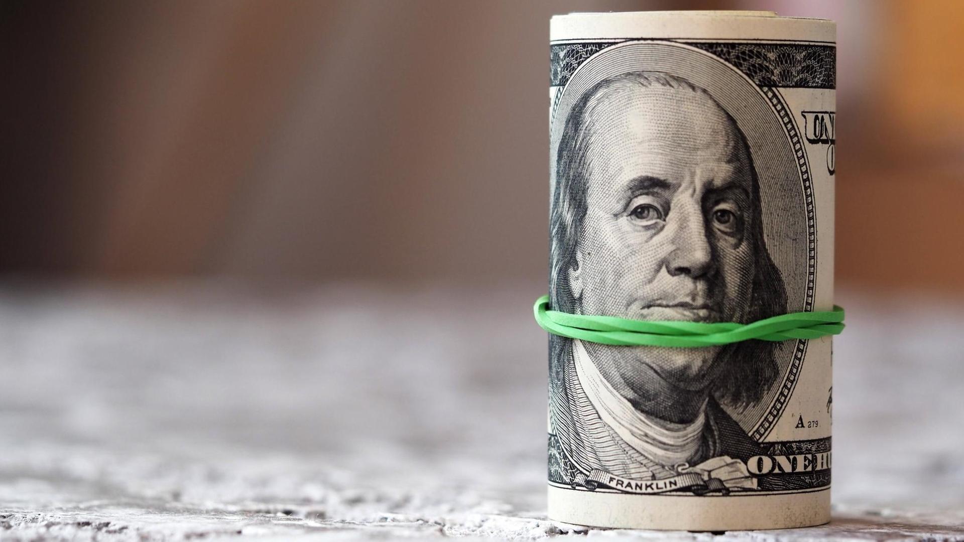 Eine Geldrolle aus Dollars, die von einem grünen Gummiband zusammengehalten wird.