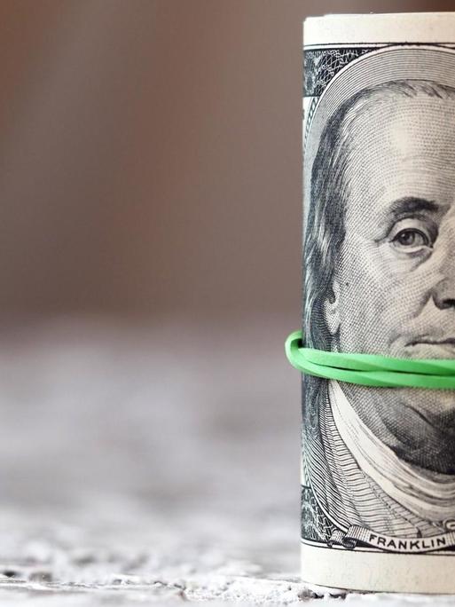 Eine Geldrolle aus Dollars, die von einem grünen Gummiband zusammengehalten wird.