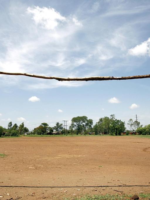 Der Fußballplatz eines Dorfes ohne nennenswerten Rasen und mit einem roh gezimmerten Tor ohne Netz aus Baumstämmen, aufgenommen am 2006 nahe der Stadt Blantyre (Provinz Mphuka) in Malawi.