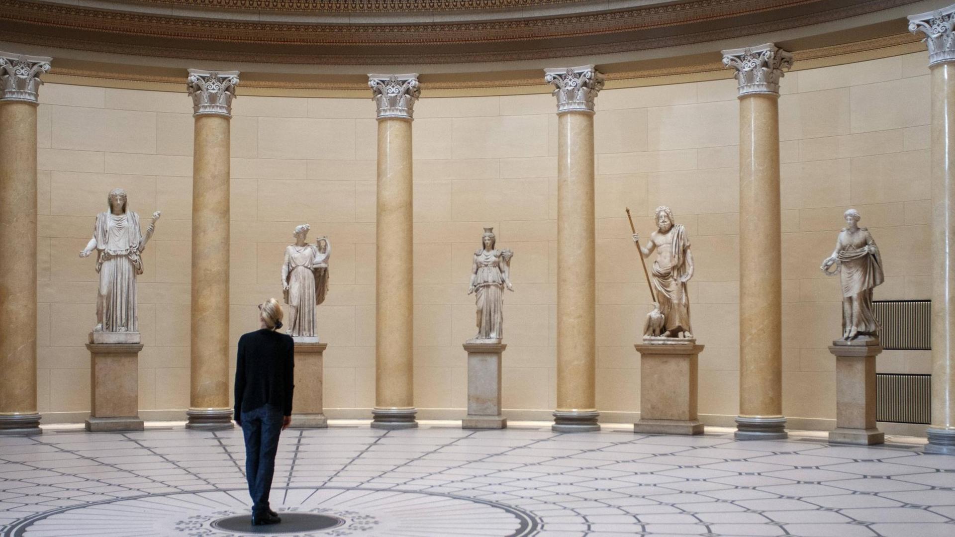 Eine Besucherin steht in einem Museum vor antiken Skulpturen