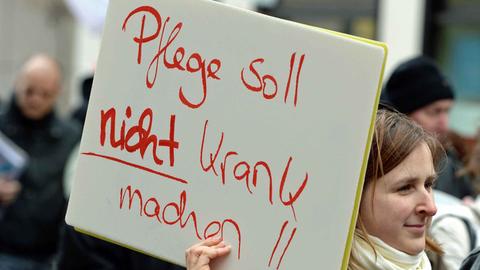 Eine Mitarbeiterin der Charité demonstriert in Berlin mit einem Plakat mit der Aufschrift "Pflege soll nicht krank machen"