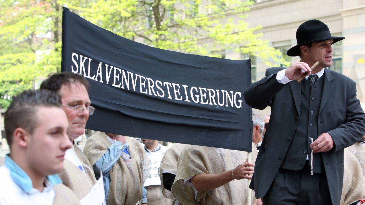 Als Sklaven verkleidete Gerüstbauer werden in Kiel symbolisch als "Arbeitssklaven" versteigert.