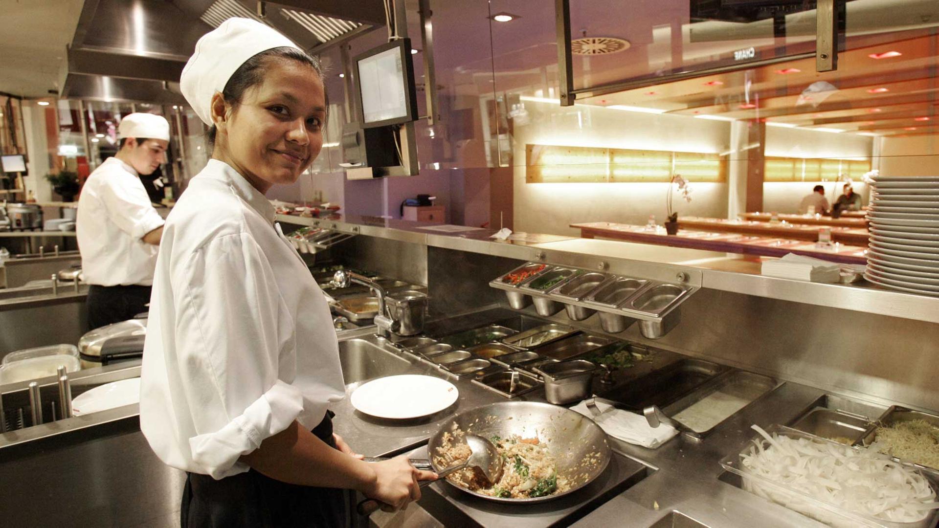 Eine Köchin rührt im Schnell-Restaurant "Cha Cha" in Hamburg den Wok auf einem Induktionsherd.
