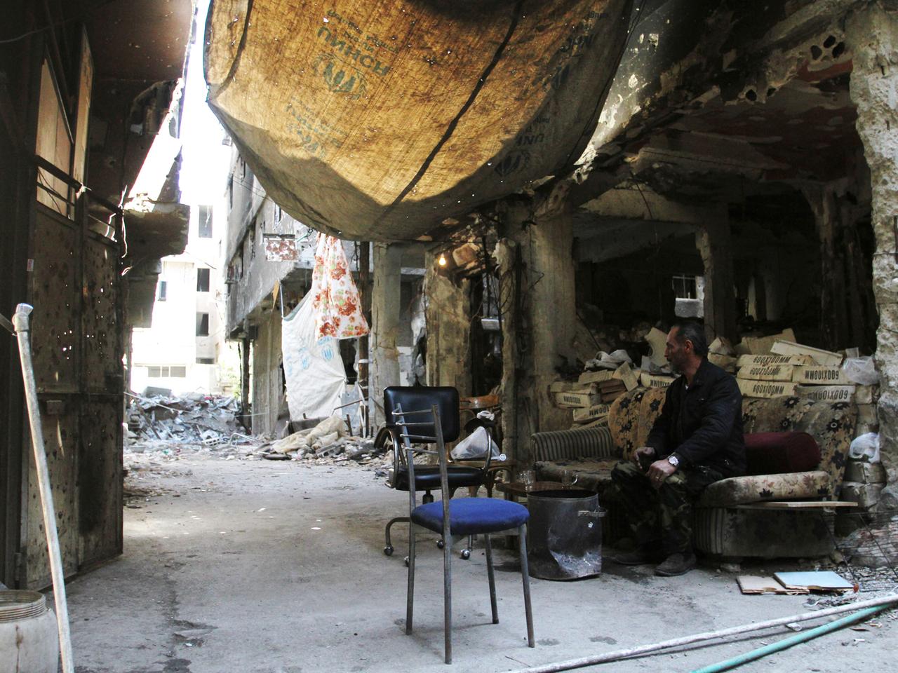 Jarmuk 2015: Ein Mann sitzt an einer Straßenecke vor einem zerstörten Gebäude