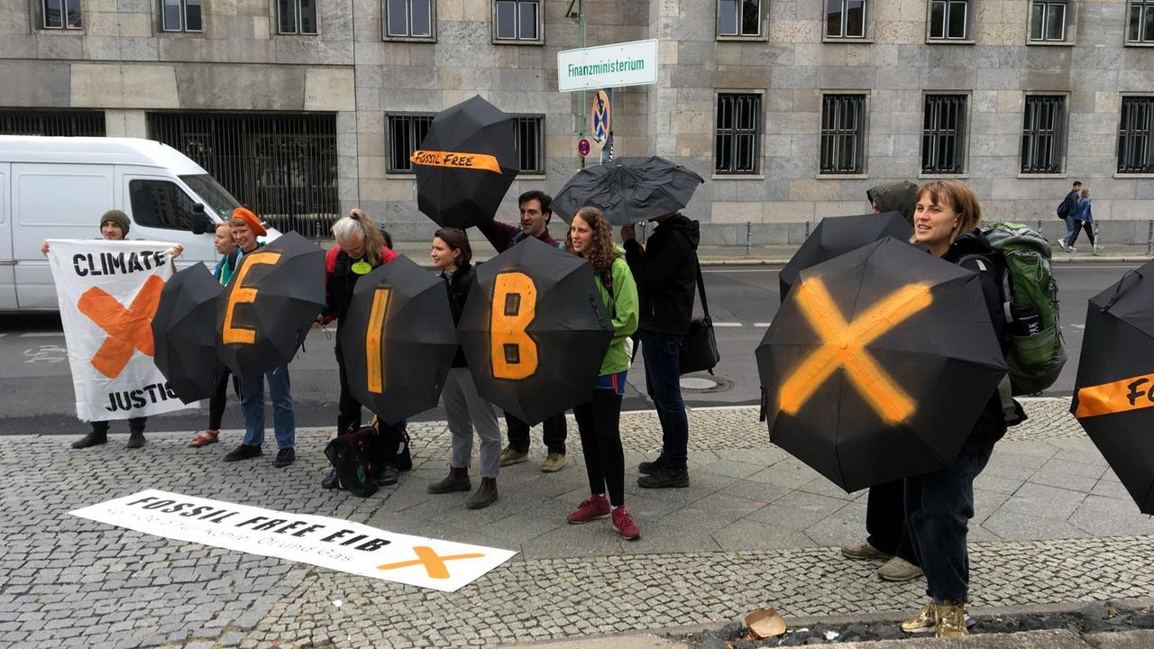 Protestierende in Schwarz mit beschriebenen Regenschirmen stehen vor dem Finanzministerium.