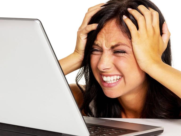 Eine junge Frau fasst sich verzweifelt an den Kopf, während sie vor ihrem Laptop sitzt