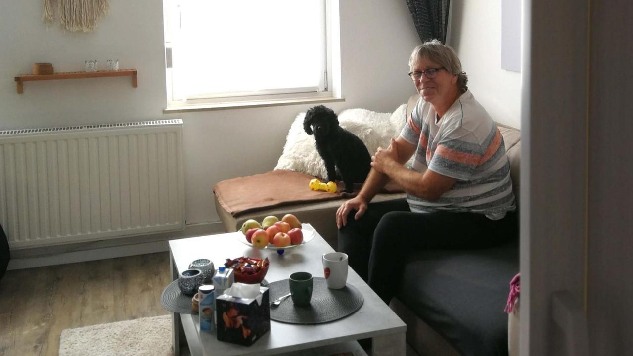 Ein Mann und ein Hund sitzen in einem Wohnzimmer auf einem Sofa.