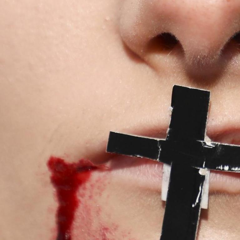 Auf einem Mund klebt ein Kreuz. Im Gesicht sind aufgemalte Wunden zu sehen. Das Bild ist ein Symbolbild für die Folgen von Homophobie in Polen.