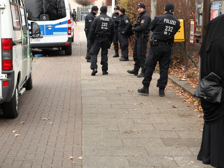 Polizeiwagen und Beamte stehen in Bremen während einer Durchsuchung vor dem salafistischen Kultur & Familien Verein (KuF) im Stadtteil Gröpelingen neben zwei Frauen, die vollkommen verschleiert sind.