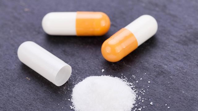 Pillen in weiß und orange und weißes Pulver auf Hinter-Grund in schwarz