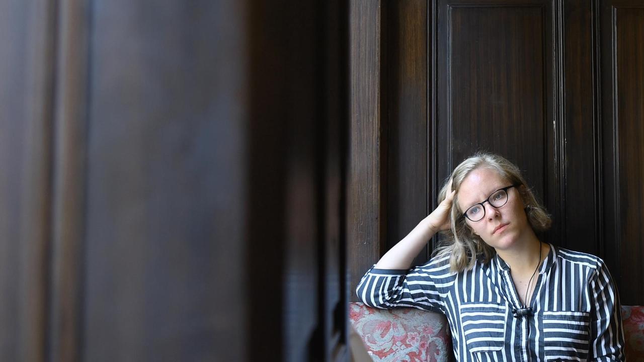 Das Bild zeigt die die österreichische Schriftstellerin Raphaela Edelbauer, die vor einer dunklen Holzwand sitzt.