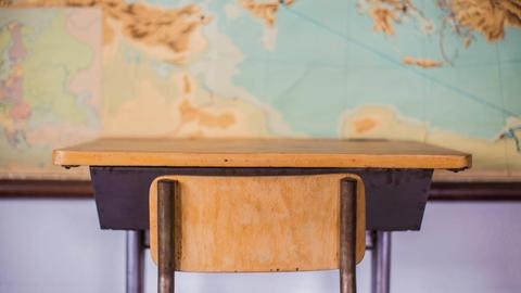 Leerer Schreibtisch in einem Klassenzimmer vor einer Weltkarte.