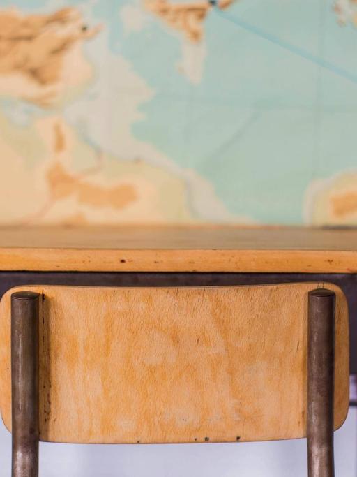Leerer Schreibtisch in einem Klassenzimmer vor einer Weltkarte.