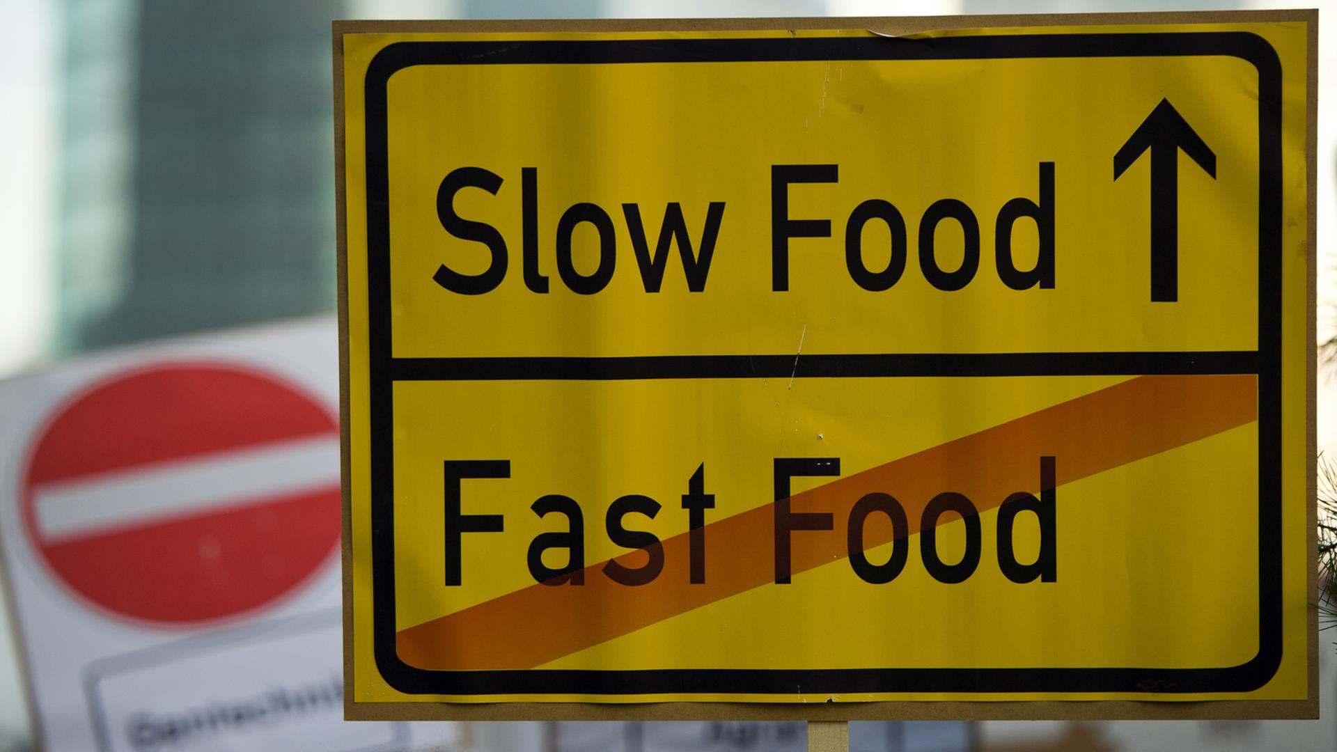Ein Schild mit der Aufschrift "Slow Food - Fast Food" bei einer Demonstration. Auf dem Schild ist Fast Food durchgestrichen.