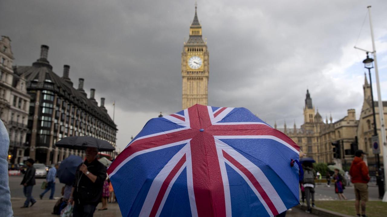 Ein Fußgänger trägt einen Schirm mit dem Union-Jack. Im Hintergrund ist Big Ben zu sehen. Ein Fußgänger trägt einen Schirm mit dem Union-Jack. Im Hintergrund ist Big Ben zu sehen.