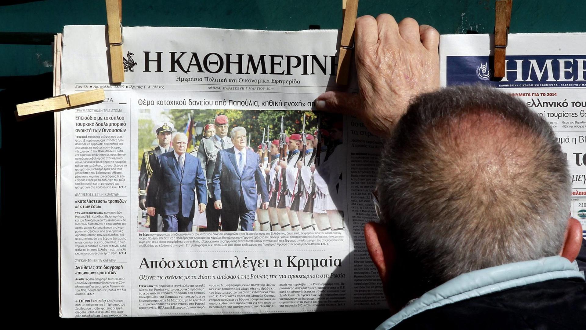 Ein Mann nimmt eine Ausgabe der griechischen Tageszeitung "Kathimerini" von einem Aushang. Auf dem Titelbild vom 07. März 2014 ist der damalige Bundespräsident Joachim Gauck beim Staatsbesuch zu sehen.