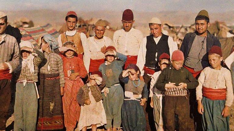 Ein Gruppenbild von Menschen unterschiedlicher Altersklassen in bunter Kleidung in einer kargen, felsigen Landschaft. 