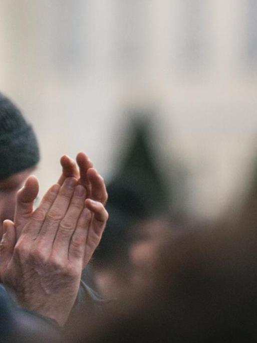 Ken Jebsen steht mit ernster Miene in einer Demonstration und klatscht.