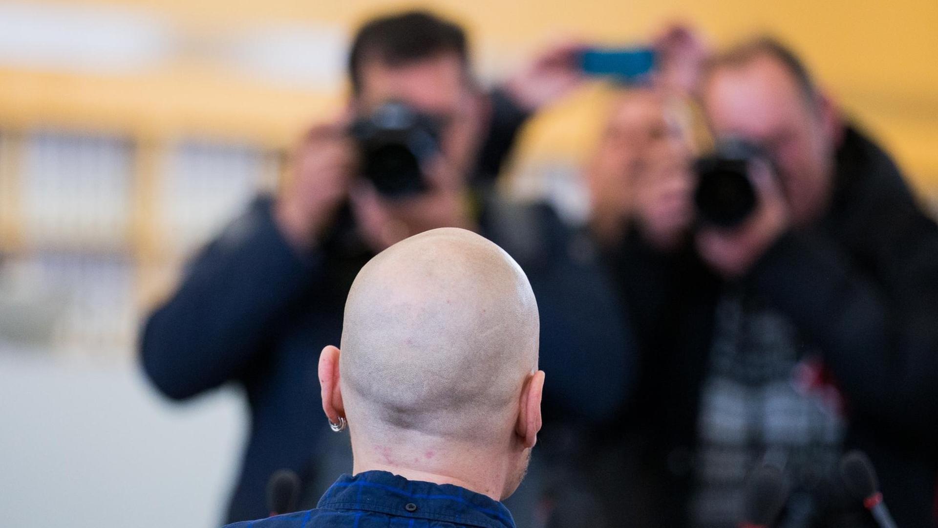 Man sieht Frank S. mit geschorenem Kopf von hinten, der von mehreren Fotografen fotografiert wird.